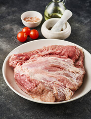 Fresh raw pork shoulder with ingredients for marinade: pepper, salt, olive oil, rosemary, garlic, view from above, close-up