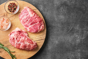 Raw pork cheeks meat on a dark gray surface with rosemary and spices. Top view. Food background . Horizontal. Space for text - obrazy, fototapety, plakaty