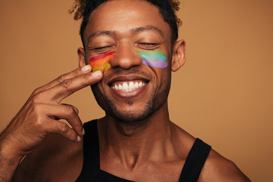 Happy black man painting LGBT flag on face