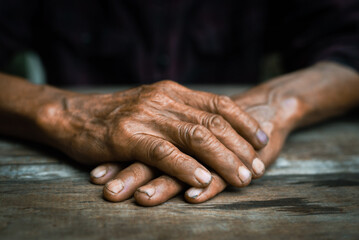 Close-up of old man's hands resting on wood. 