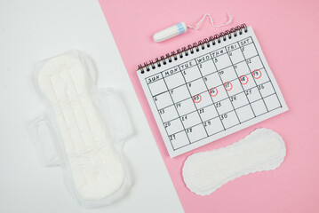 Top view of a calendar of women's critical days with pads and accessories on a white and pink background with copy space.