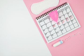 Top view of a calendar of women's critical days with pads and accessories on a white and pink background with copy space.