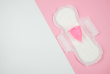 Top view of pad and menstrual cup on white and pink background