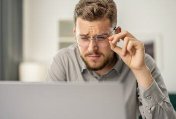 Young bearded man look closely at laptop, focused man use computer, coder working at home