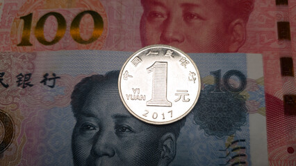 A coin with a denomination of one Chinese yuan which lies on paper bills of one hundred yuan and ten yuan. 1 yuan shot close up