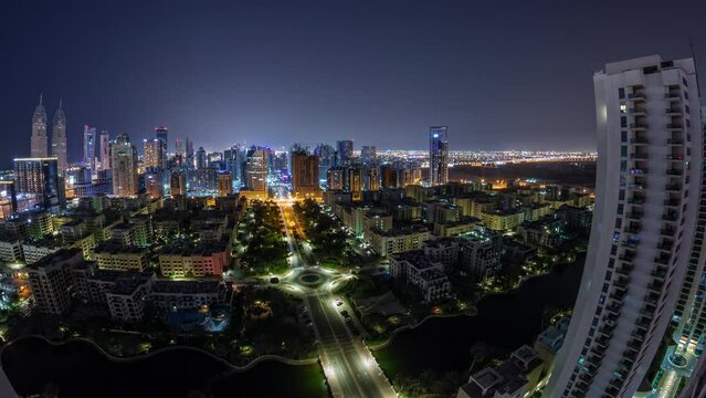 Panorama with skyscrapers in Barsha Heights district and low rise buildings in Greens district aerial timelapse during all night. Dubai skyline with traffic and lights swithcing off
