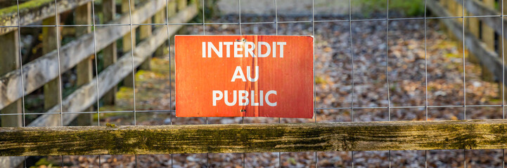 Sign indicating "forbidden to the public" in French on a fence of a wooden footbridge in a forest on an autumn day