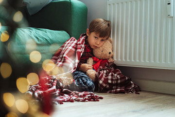 cute little boy wrapped id plaid sitting by heater