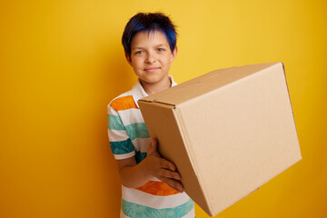 Fototapeta Teenage boy holding blank cardboard box over isolated yellow background, delivery concept obraz
