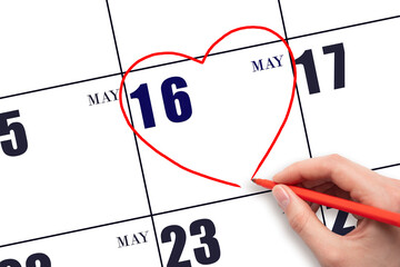 A woman's hand drawing a red heart shape on the calendar date of 16 May. Heart as a symbol of love.