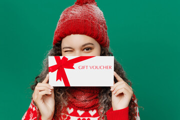 Merry young woman in red warm sweater hat posing hold cover mouth with gift certificate coupon...