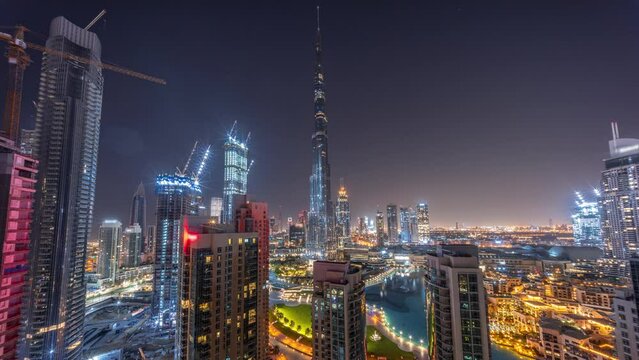 Dubai Downtown cityscape with tallest skyscrapers around aerial panoramic timelapse during all night. Construction site of new towers and busy roads with traffic from above. Lights turning off