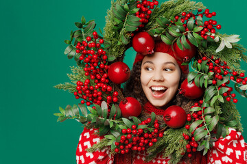 Close up fun cool smiling merry young woman wear Christmas wreath on head posing look aside on workspace area isolated on plain dark green background Happy New Year 2023 celebration holiday concept.