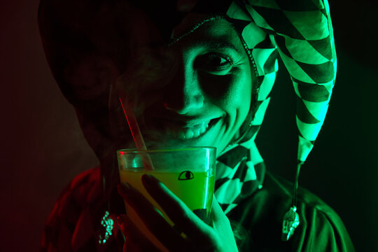 Woman dressed as a harlequin smiling holding a drink with smoke at a costume Halloween party.
