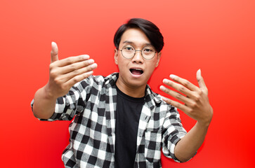 Asian young man wearing glasses inviting to come with hand isolated over red background. welcoming gesture. billboard advertisment model concept.