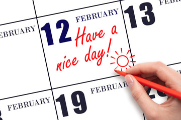 The hand writing the text Have a nice day and drawing the sun on the calendar date February 12