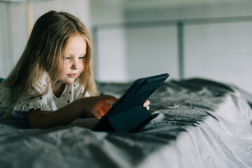 Cute little girl use digital tablet while lying in bed