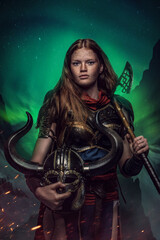 Obraz premium Shot of female warrior with helmet and axe dressed in armor against polar lights.