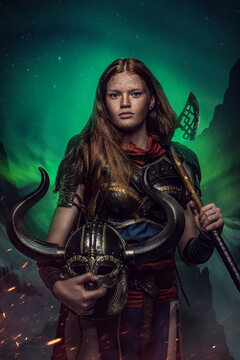 Shot of female warrior with helmet and axe dressed in armor against polar lights.