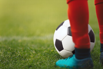 Football ball and footballer in red socks and cleats standing on a grass pitch. Player kicking a...