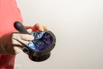close-up of a woman's hand with a latex glove making a mixture of a blue chemical to dye hair with...