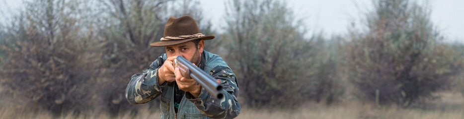 Fototapeta premium Hunter man in camouflage with a gun during the hunt in search of wild birds or game.