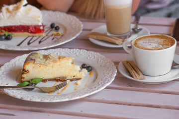Table for two in the street coffee shop. Plate with piece of cheesecake and blueberries, cup of cappuccino and latte.