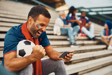 Passionate soccer fan cheering while watching match on mobile phone.