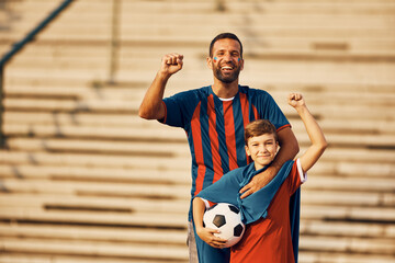 Happy boy and his father cheering during soccer world championship and looking at camera.