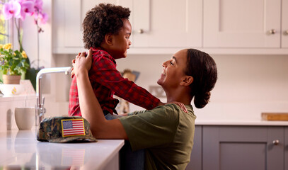 American Army Mother In Uniform Home On Leave Hugging Son In Family Kitchen