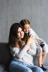 Close up happy attractive mother hugging cute preschool daughter. Smiling young mom closed eyes embracing little girl enjoying free time together sitting on couch at home.