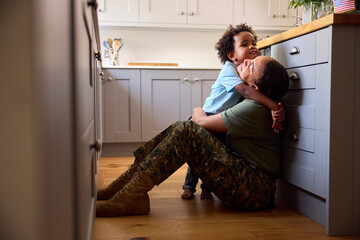 American Army Mother In Uniform Home On Leave Hugging Son Sitting On Floor In Family Kitchen