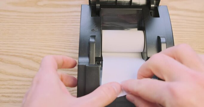 Replacing the thermal paper roll in a receipt printer. First person view, hands inserting the roll into the printer.