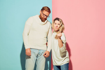 Studio shot of couple of young emotional man and woman isolated over blue and pink background. Care, protection