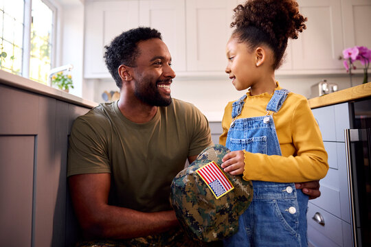 Daughter Holding Cap Of American Army Father In Uniform Home On Leave In Family Kitchen