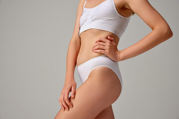 Fototapeta na wymiar Cropped image of sportive female body in white underwear isolated over grey studio background. Sportive lifestyle
