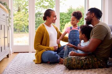 Army Family With Pregnant Mother Sitting On Floor In Lounge At Home