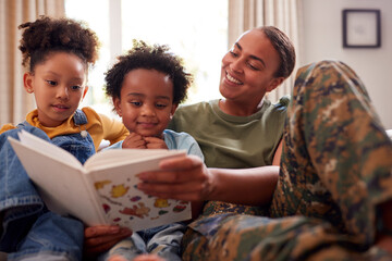 Army Mother In Uniform Home On Leave With Children Reading Book On Sofa Together