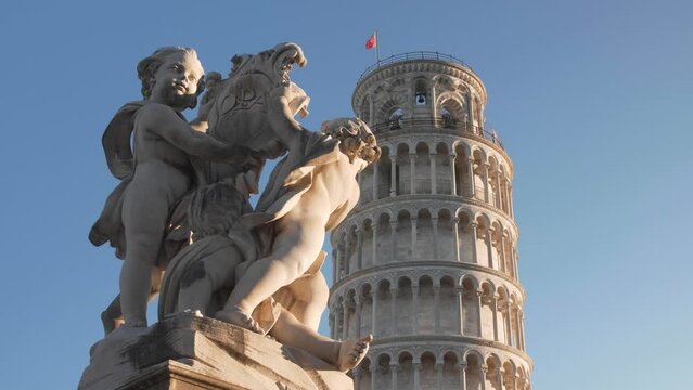 close up of the Leaning tower of pisa with clear blue sky in the morning during golden hour with statue in the foreground filmed with a gimbal and a dolly movement in tuscany, italy