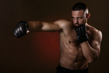 Fototapeta na wymiar Studio portrait of fighting muscular man in black fighting gloves posing on dark background. The concept of mixed martial arts. Brutal bodybuilder energy and power boxing.