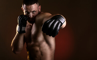 Studio portrait of fighting muscular man in black fighting gloves posing on dark background. The...