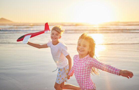 Children running with airplane toys on beach together for wellness, exercise and healthy development on sunset horizon and ocean waves. Kids having fun and playing for outdoor summer holiday portrait - Powered by Adobe