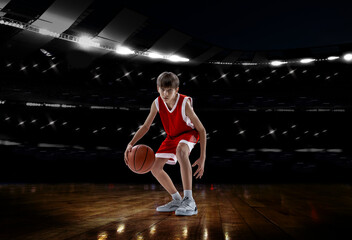 Fototapeta na wymiar Portrait of teen boy, professional basketball player isolated over sport stadium background. Concentrated sportsman