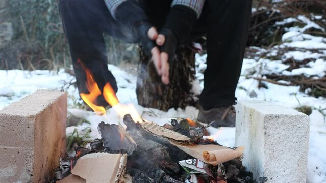 A homeless warms his hands over an outdoor fireplace
