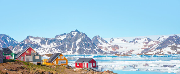 Panoramic view of colorful Kulusuk village in East Greenland - Kulusuk, Greenland - Melting of a iceberg and pouring water into the sea - obrazy, fototapety, plakaty