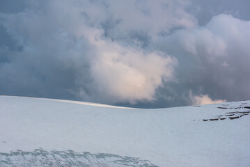 Dramatic landscape with glacier on sunlit high snow mountain top under cloudy sky at sunset....