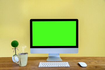 Modern computer with green screen in office. Mockup design desktop computer in office on wooden table with keyboard and Coffee cub, Work place concept