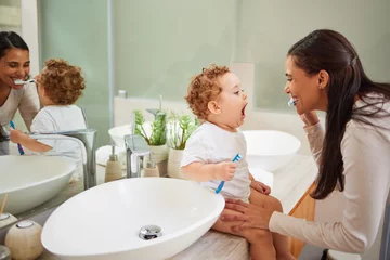 Ingelijste posters Tandarts Mom teaching baby to brush its teeth, on the bathroom counter in home and a clean smile on her face. Healthy oral hygiene for kid means using child friendly toothpaste, toothbrush and dental routine  © Alexis Scholtz/peopleimages.com