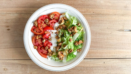 bowl of vegetable salad with chinese cabbage, tomato with mayonnaise dressing and granola as topping. isolated on wooden background.