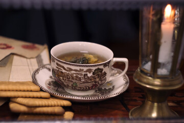 Holiday evening at home - porcelain cup of best herbal tea, antique candle in candlestick, old letters and jar of honey